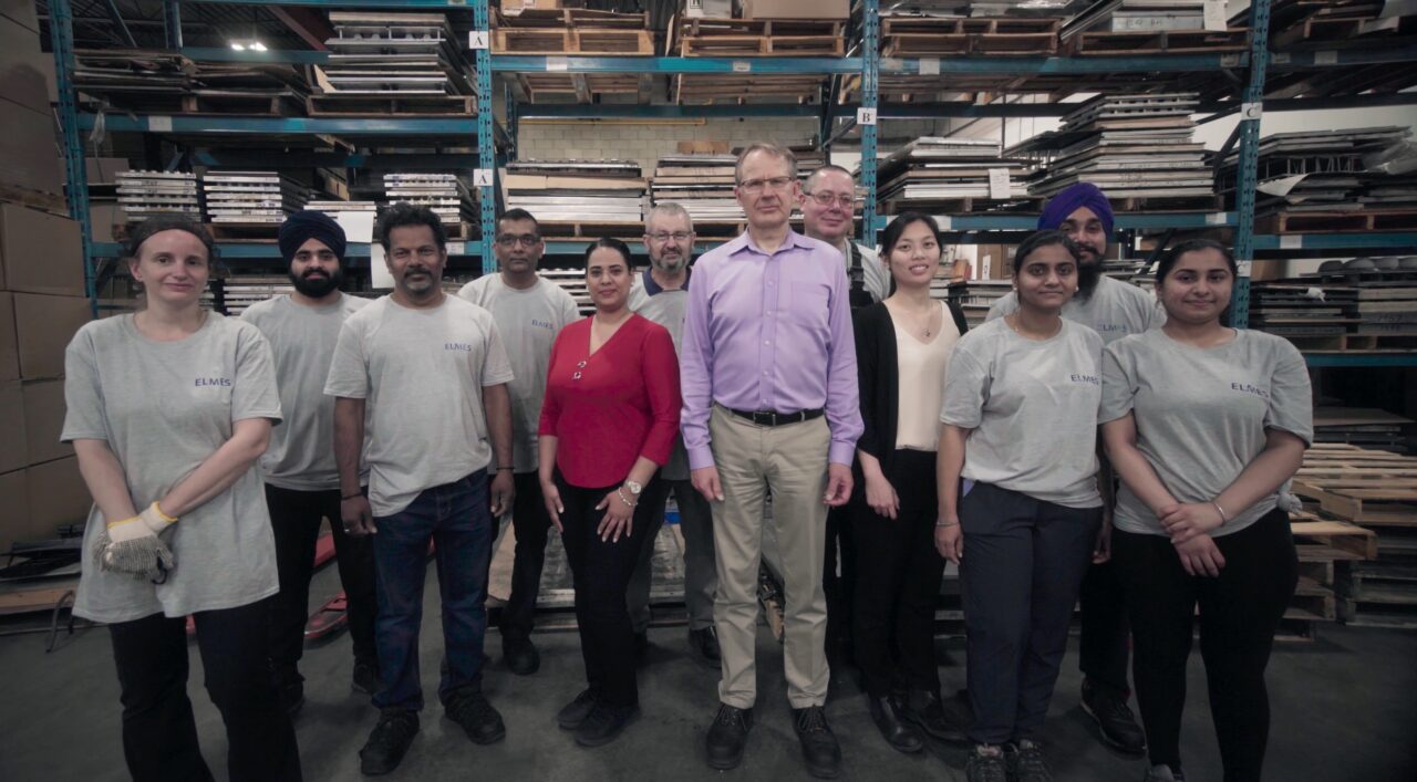 A group shot of Elmes Packaging staff standing in front of warehouse shelves